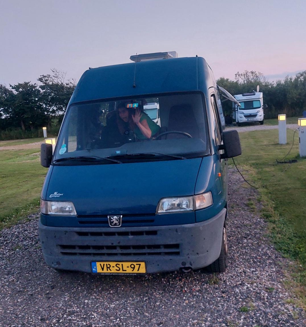 De camper staat op z'n plek, Suzan zwaait vrolijk vanuit de bus.
