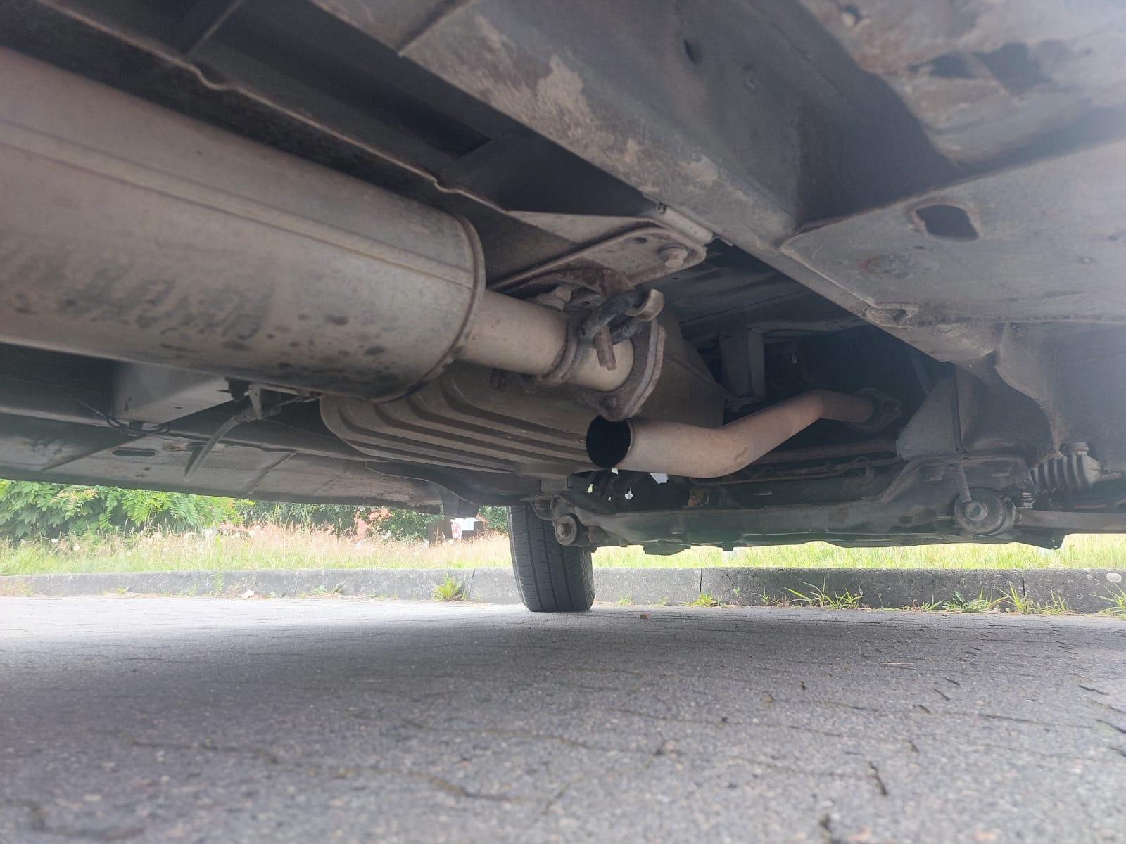 Foto van de onderkant van de bus waar het loshangende gedeelte van het uitlaatsysteem te zien is
