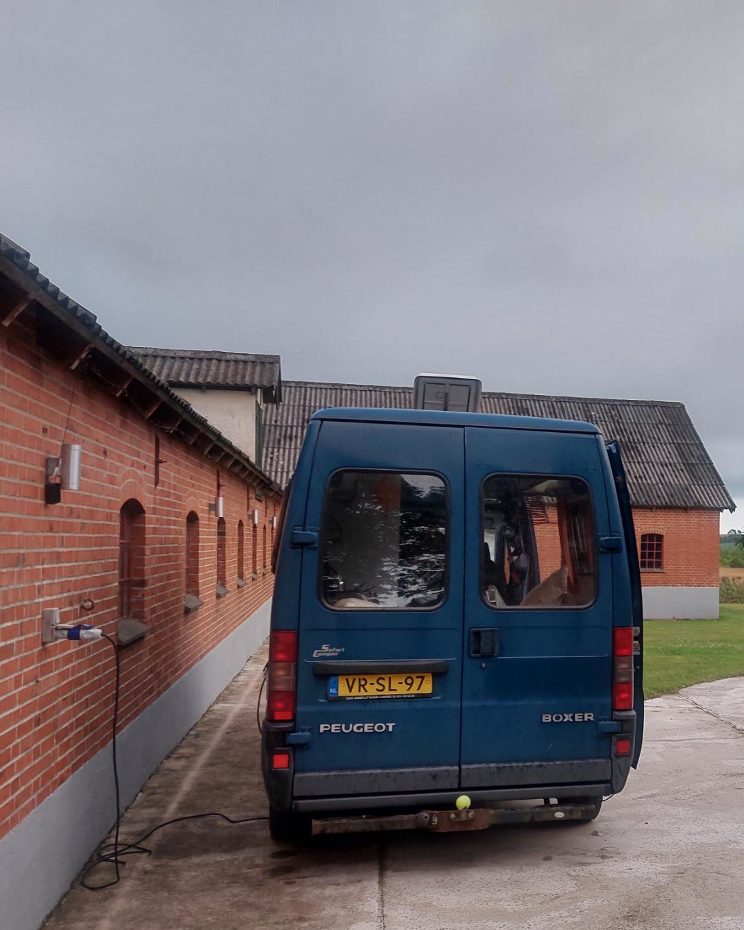 De camper staat helemaal alleen naast een schuur